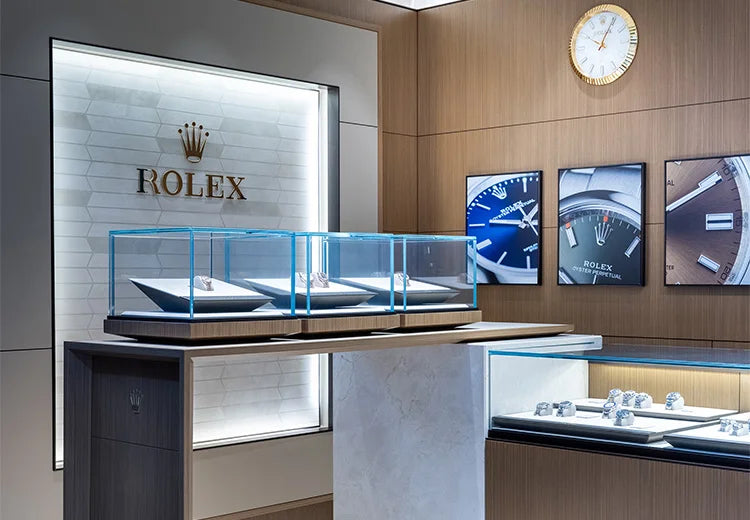 A luxury Rolex watch and jewelry display showroom with illuminated glass cases, wood-paneled walls, framed watch imagery, and a Rolex logo on a backlit wall panel.