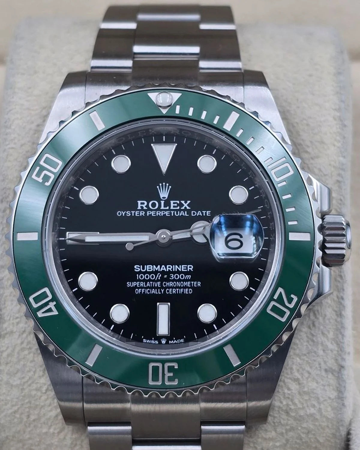 Rolex Submariner Date watch with a black dial, green bezel, and stainless steel Oyster bracelet, displayed on a beige cushion.